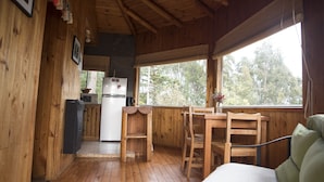 L’intérieur d’un chalet en bois comprend un coin cuisine, une table à manger et une fenêtre donnant sur la forêt.