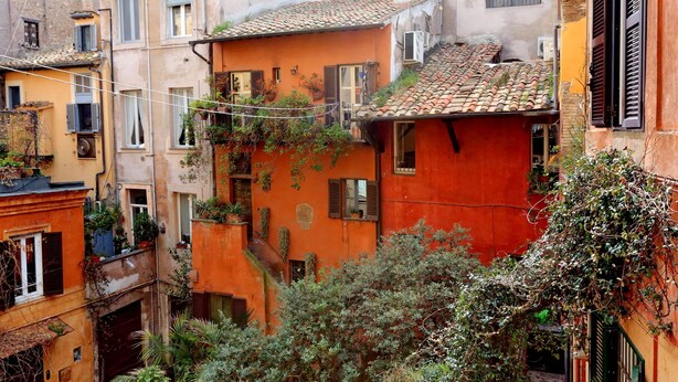 A narrow street with closely packed buildings, some with balconies and potted plants. - Pellegrino - WR Apartments (Rome)