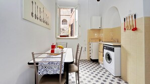 A compact kitchen with a washing machine, a dining table with chairs, and a window with a view of an alley. - Pellegrino - WR Apartments (Rome)