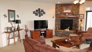 Una sala de estar con chimenea de piedra, sofás de cuero, una mesa de centro de madera y un televisor de pantalla plana.