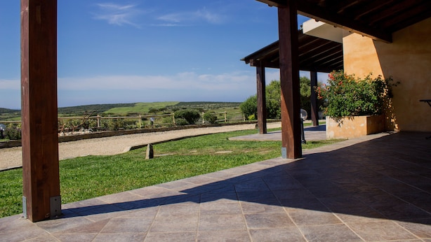 Un espacio al aire libre cubierto, con suelo de piedra, vigas de madera y vistas al campo.