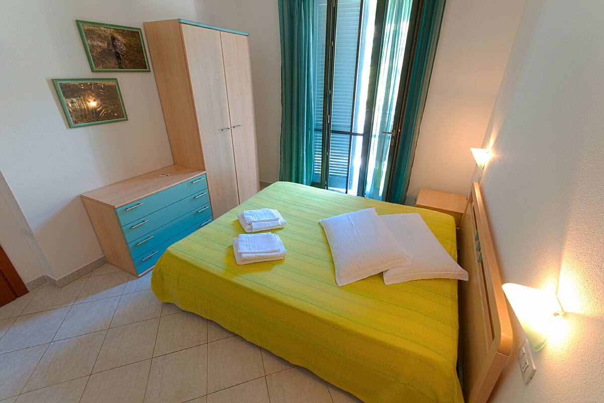 A bedroom with a bed, a wardrobe, a bedside table, and a wall-mounted light.