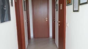 Un pasillo con una puerta de madera al final, suelo de baldosas e imágenes enmarcadas en las paredes.