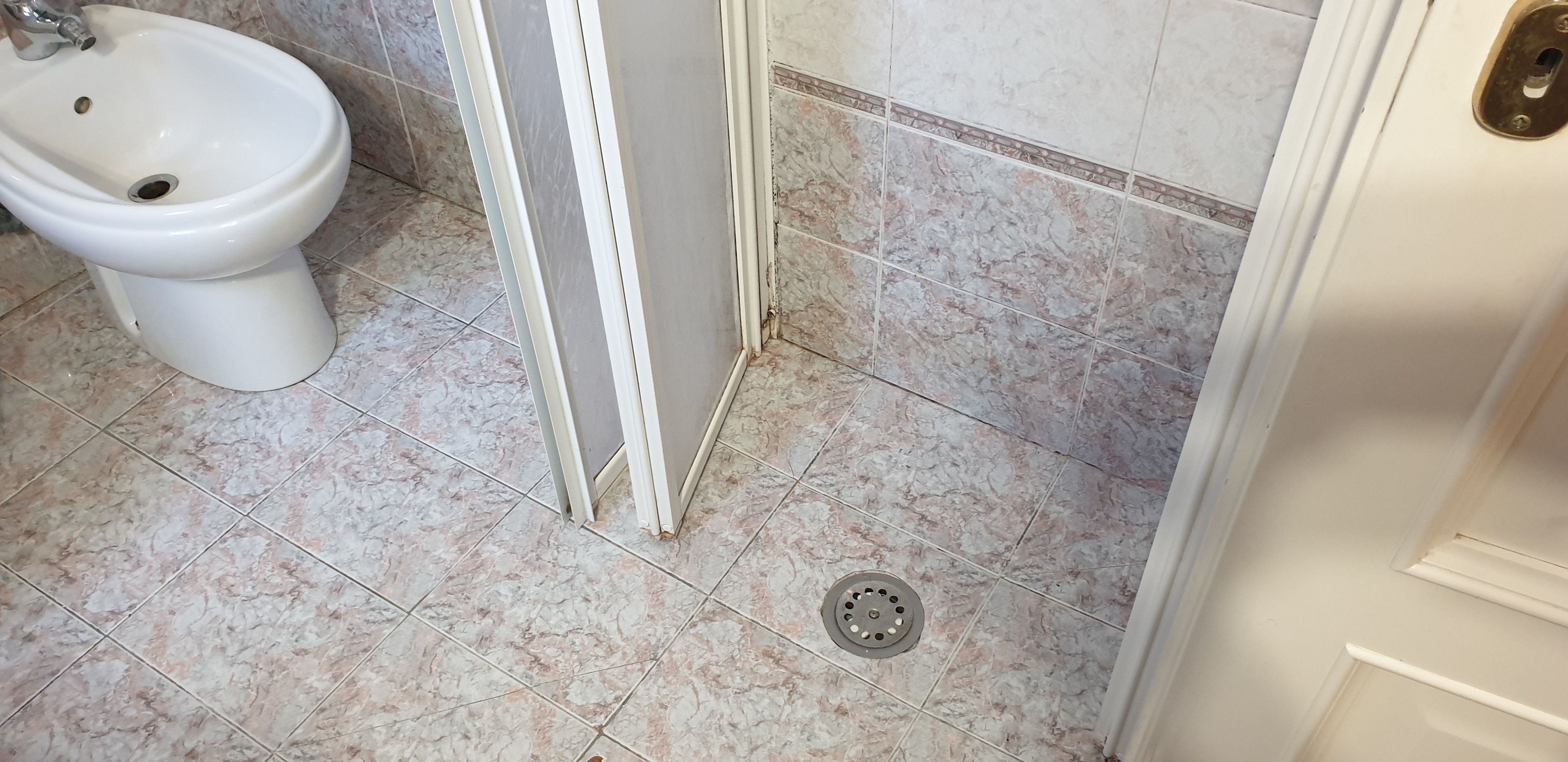 A bathroom with a bidet, a shower door, and a marble floor.
