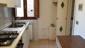 A compact kitchen with a gas stove, stainless steel sink, and a window with a view of a brick wall. - Sapienza Time (Siena)