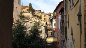 A narrow street with buildings on either side, featuring balconies and a mix of brick and plaster facades. - Sapienza Time (Siena)