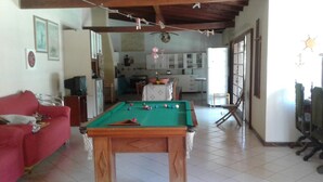 Una sala de estar con mesa de billar, un sofá rojo y una cocina al fondo.