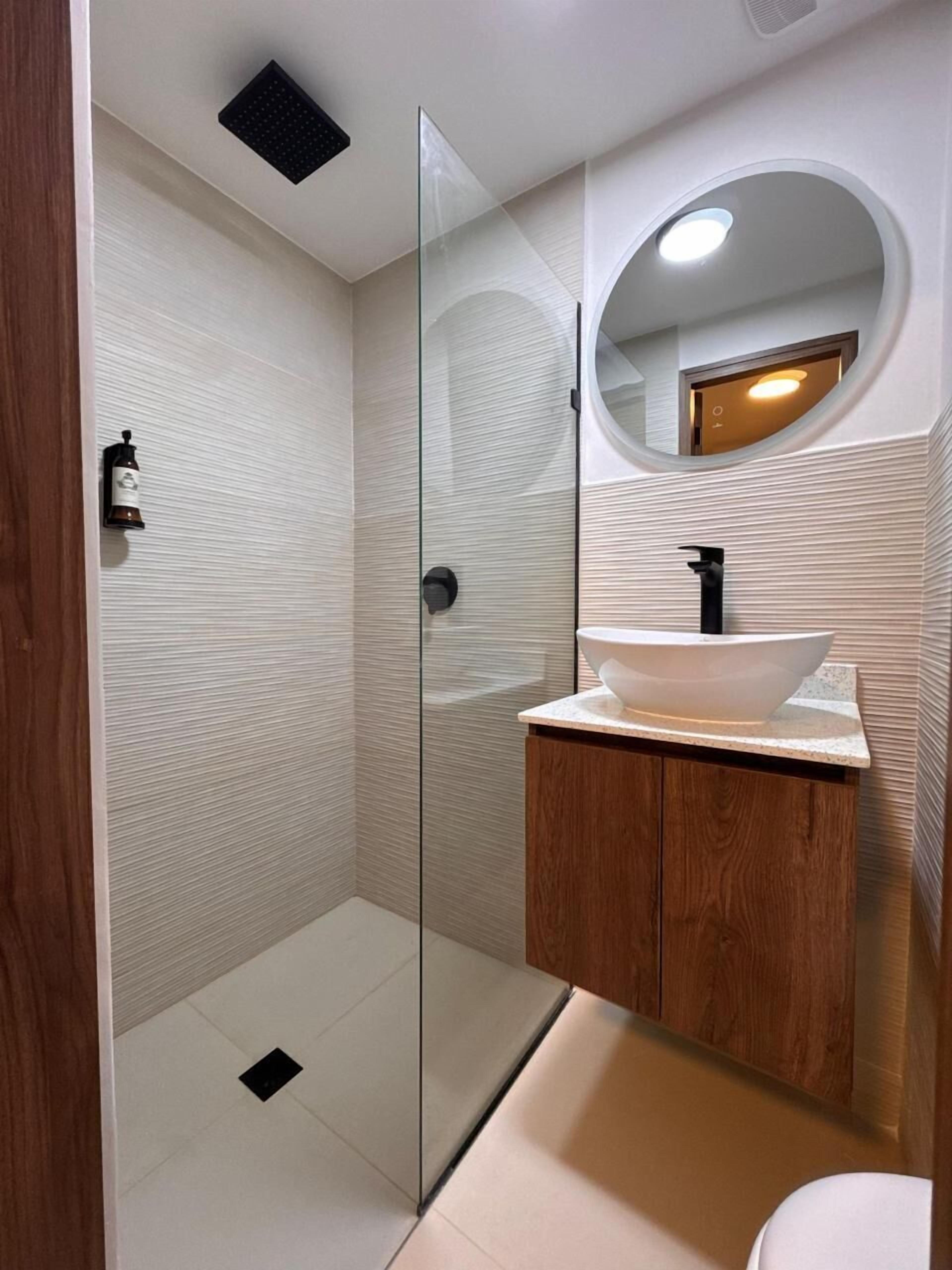 A modern bathroom with a glass shower enclosure, a wooden vanity, and a round mirror.