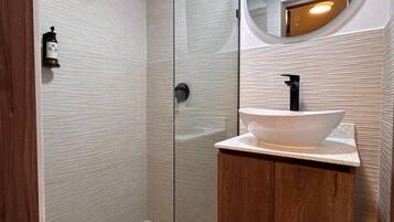 Un baño moderno con cabina de ducha de vidrio, tocador de madera y espejo redondo.