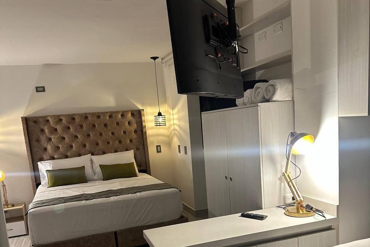 A modern hotel room with a large bed, a smaller bed, a desk, a wardrobe, and a television mounted on the wall.