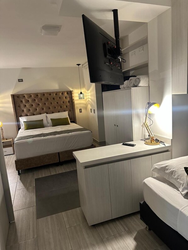 A modern hotel room with a large bed, a smaller bed, a desk, a wardrobe, and a television mounted on the wall. - Hotel Balcones del Estadio (Medellín)