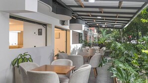 A modern outdoor seating area with tables and chairs, surrounded by potted plants and a view of the street. - Hotel Balcones del Estadio (Medellín)