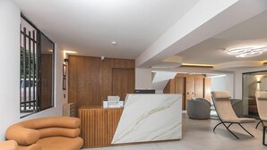 A modern reception area with a wooden reception desk, a marble display, and contemporary seating. - Hotel Balcones del Estadio (Medellín)