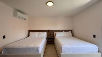 A room with two single beds, a ceiling light, and an air conditioning unit on the wall.