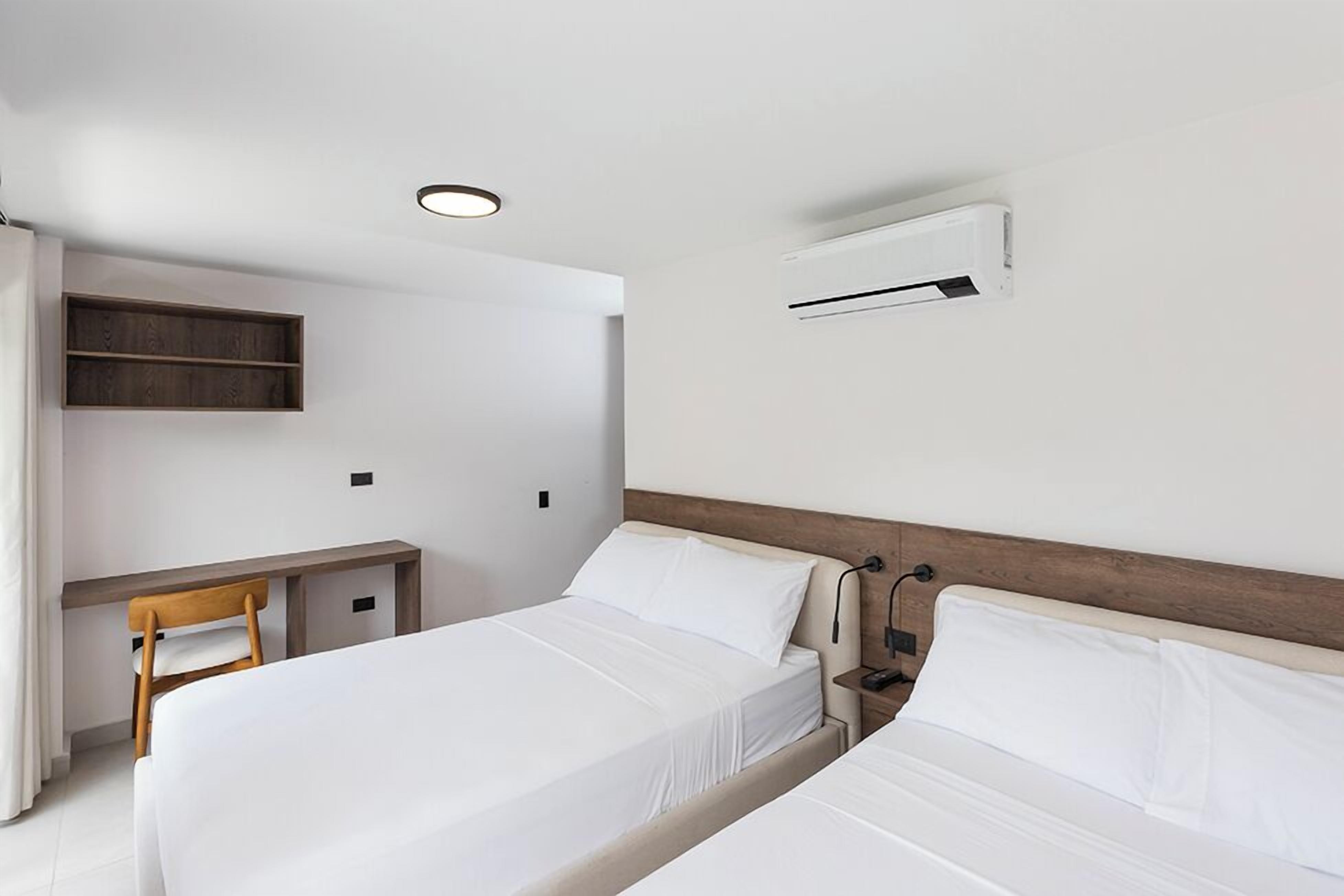 A modern hotel room with two beds, a desk, and an air conditioning unit.