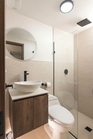 A modern bathroom with a white vessel sink, a toilet, and a glass shower enclosure. - Hotel Balcones del Estadio (Medellín)