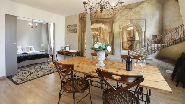 A dining area with a wooden table, chairs, a chandelier, and a large mural on the wall. - Nature & Chateaux à Chinon (Chinon)