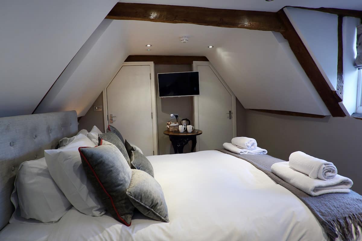 A bedroom with a large bed, a flat-screen TV mounted on the wall, and a small table with a coffee pot and cups.