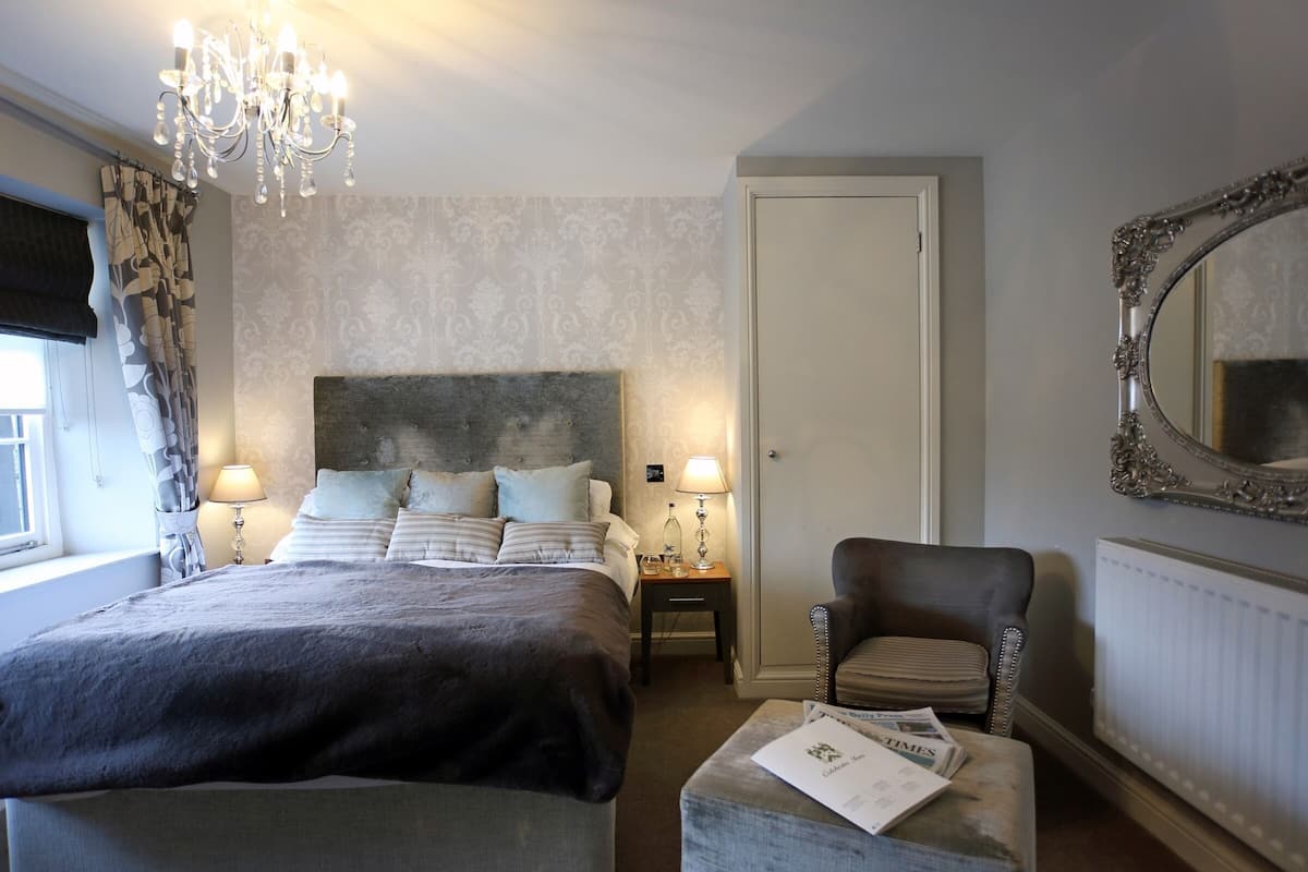A bedroom with a large bed, a chair, a nightstand, a mirror, and a chandelier.