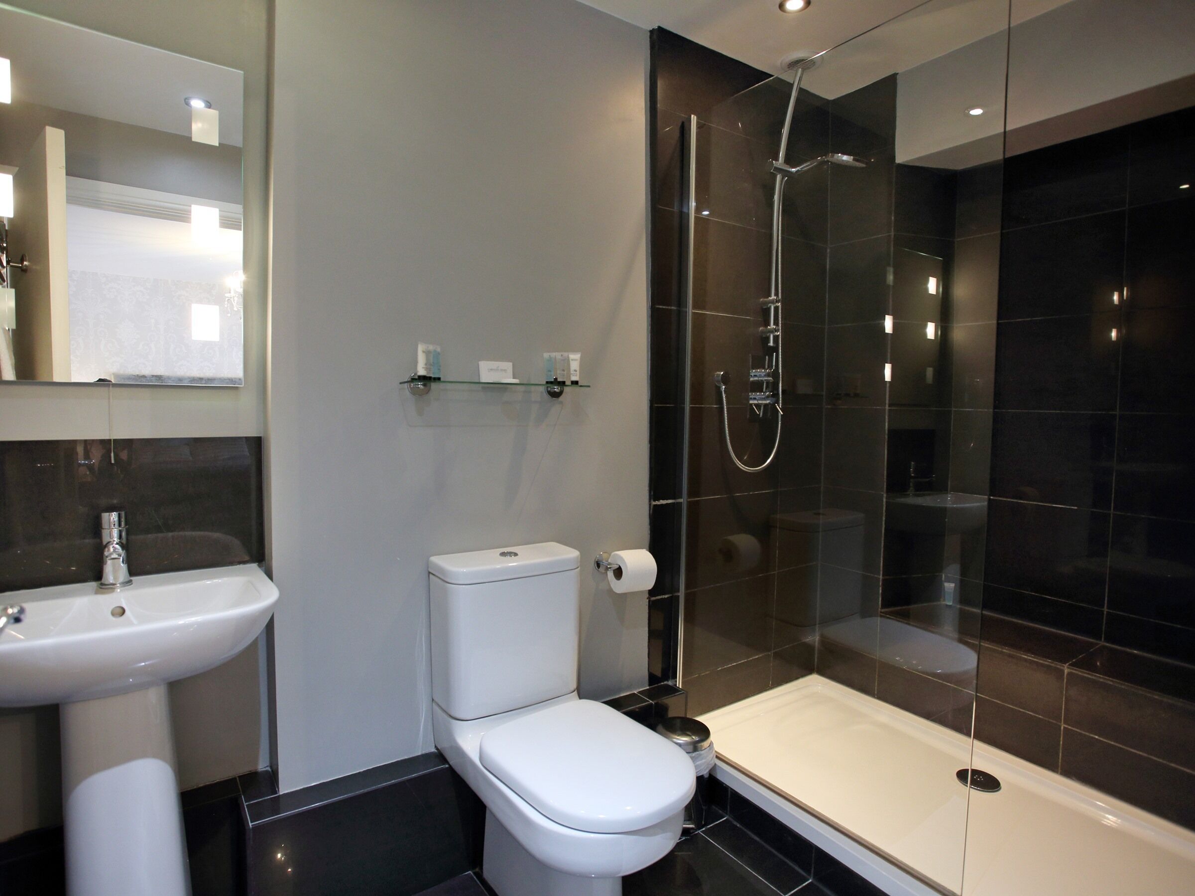 Un baño moderno con inodoro, lavamanos y ducha con mampara de vidrio.