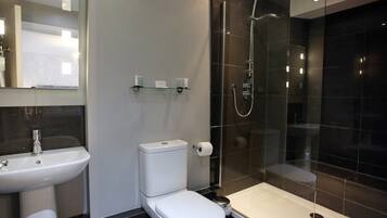 Un baño moderno con inodoro, lavamanos y ducha con mampara de vidrio.