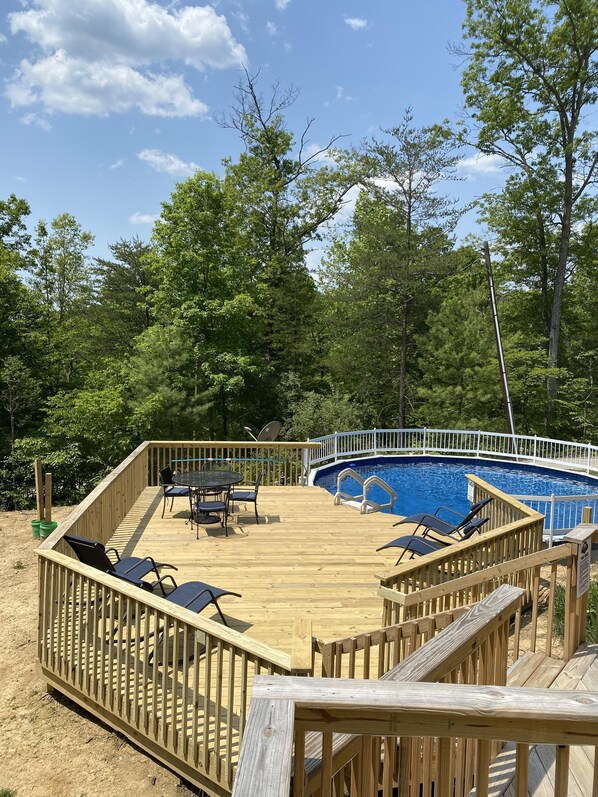 Eine Holzterrasse mit einem Pool, umgeben von Bäumen.