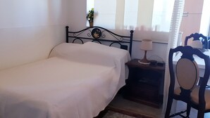 A single bed with a white bedspread, a nightstand with a lamp, and a chair with a wooden frame. - Porta Camollia Apartment (Siena)