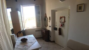 A dining area with a table, chairs, a window, a radiator, a door with a mirror, and a wall-mounted decoration. - Porta Camollia Apartment (Siena)