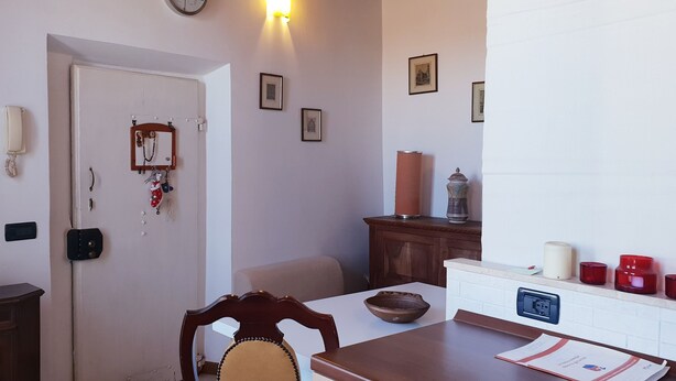 A dining area with a wooden table, chairs, a wall-mounted telephone, framed pictures, and a cabinet with candles. - Porta Camollia Apartment (Siena)