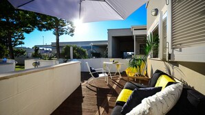 An outdoor patio with a wooden deck, white walls, and a yellow umbrella providing shade. - Residence Cala Paura - Vecchio Frack (Polignano a Mare)