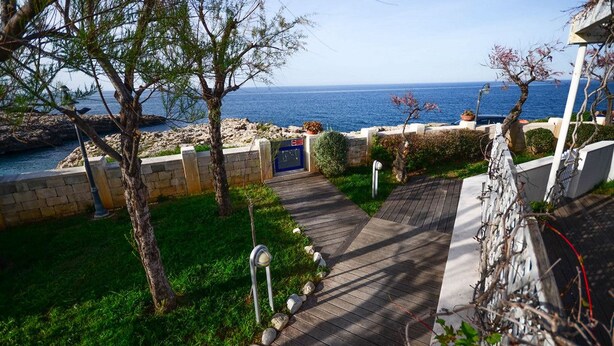 A coastal property with a paved pathway leading to a gate, surrounded by greenery and a view of the sea. - Residence Cala Paura - Vecchio Frack (Polignano a Mare)