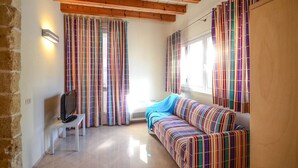 A cozy room with a striped sofa, a television on a small table, and colorful curtains. - Residence Cala Paura - Vecchio Frack (Polignano a Mare)