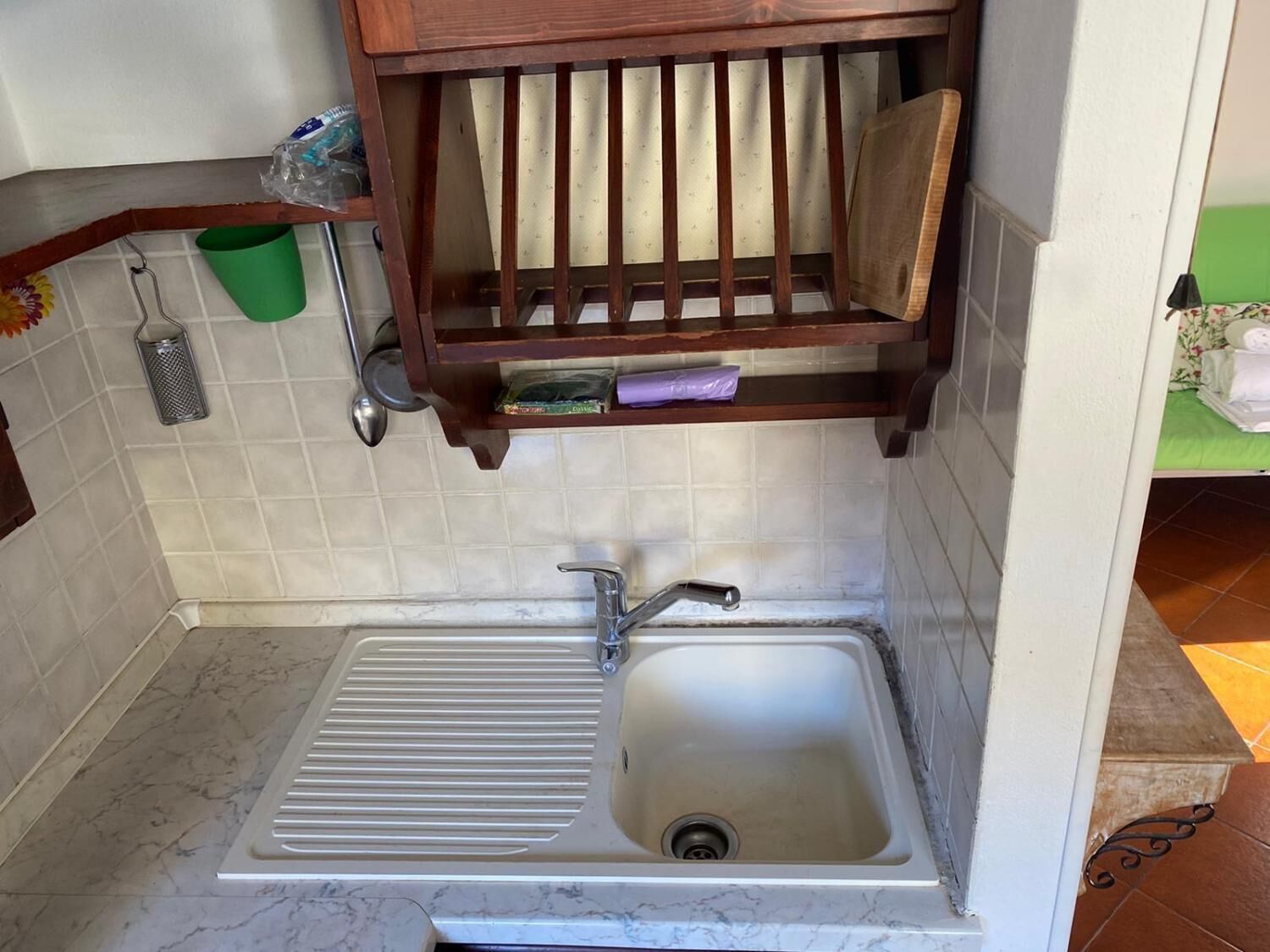 Una cocina con un lavabo, un estante de madera encima y un cubo verde en la pared.
