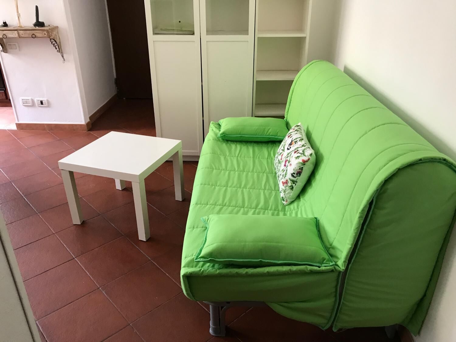 Un sofá verde con cojines estampados, una mesa blanca y un suelo de baldosas.