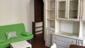 Une pièce avec un canapé vert, une table blanche, une chaise blanche et un meuble avec des portes en verre.