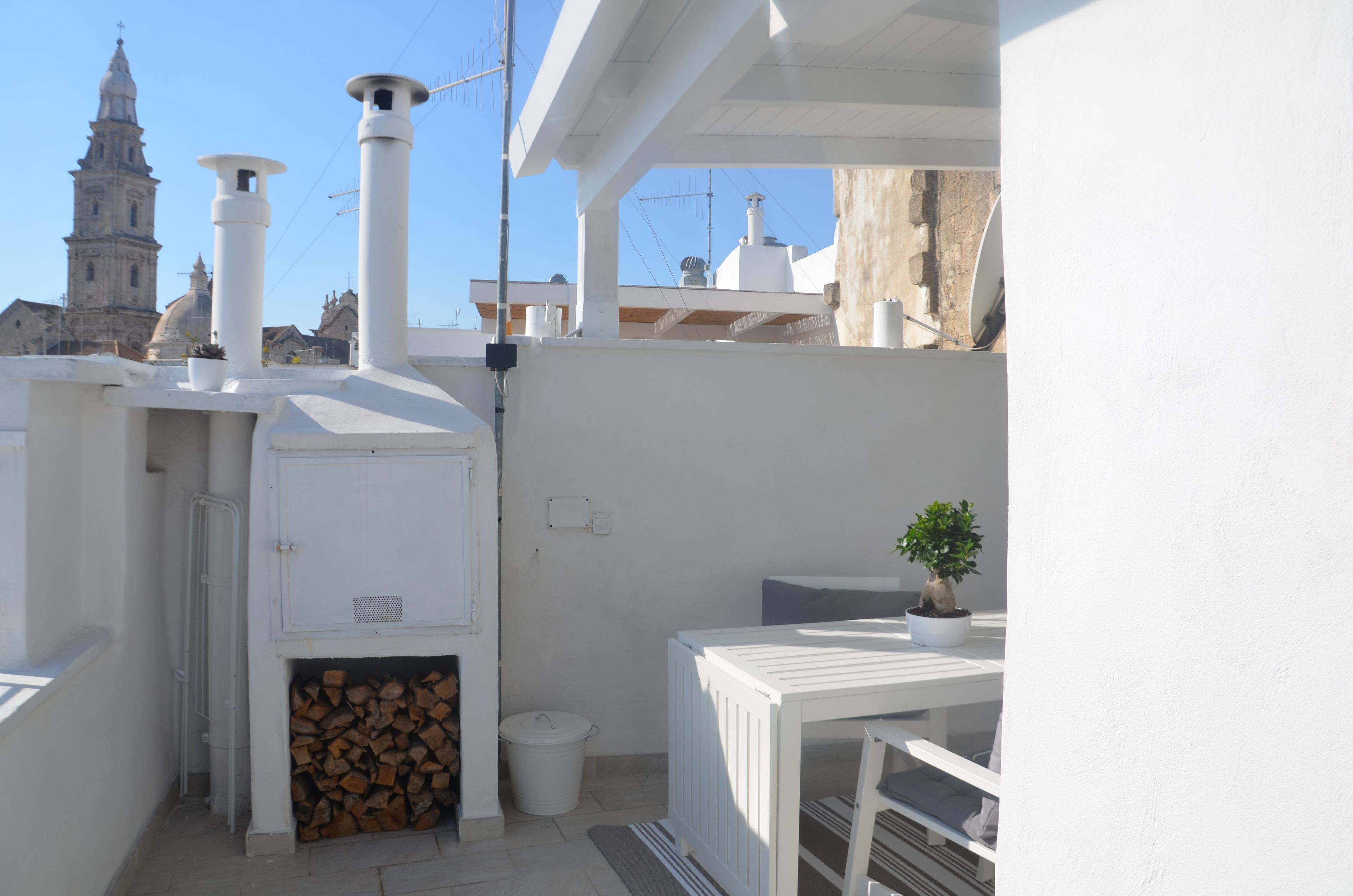 A rooftop terrace with a wood stove, a potted plant, and a view of a historic church tower.