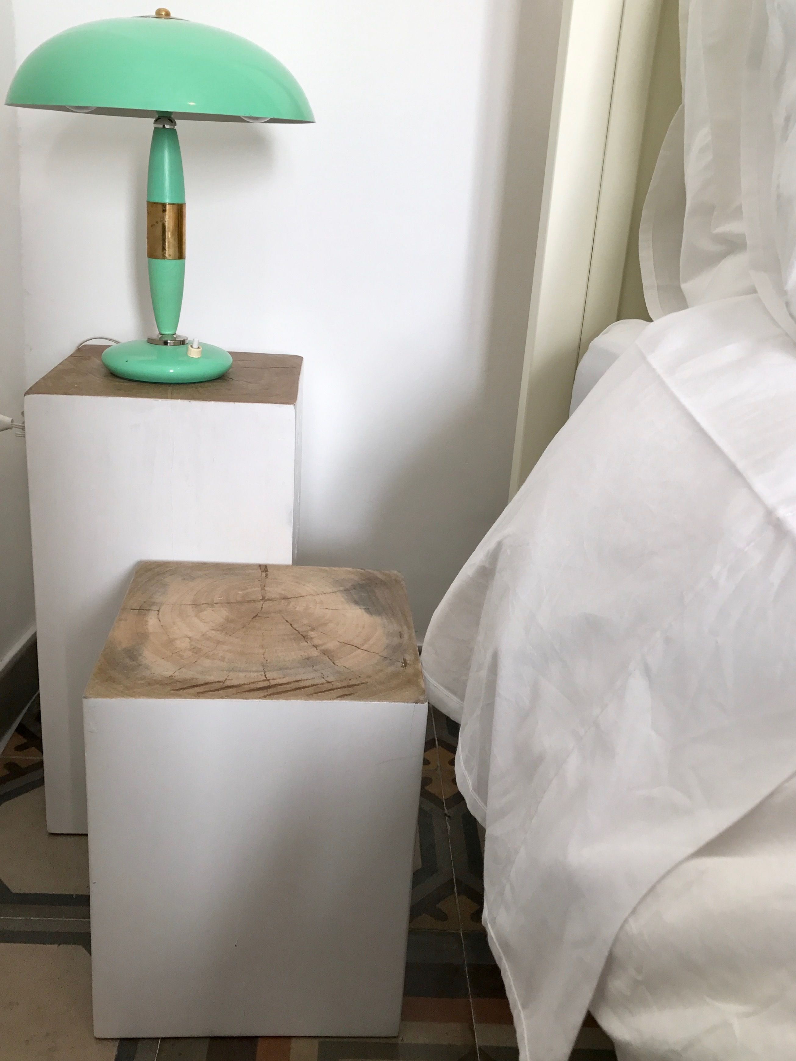 A room with a white bed, a white nightstand with a green lamp, and a wooden nightstand.