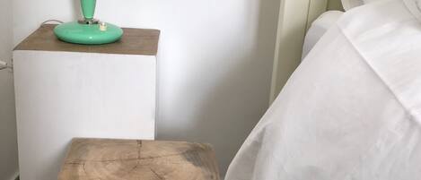 A room with a white bed, a white nightstand with a green lamp, and a wooden nightstand.