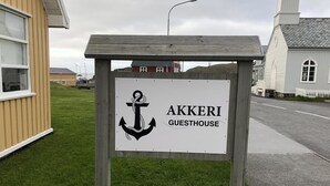 A sign for the Akkeri Guesthouse, featuring a wooden structure with a white background and a black anchor symbol. - Akkeri Guesthouse (Stykkisholmur)