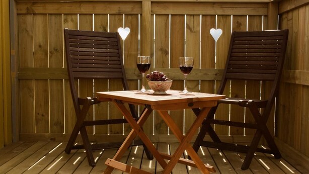 Two wooden chairs and a table with a bowl of grapes and two glasses of red wine, set against a wooden fence with heart-shaped cutouts. - Akkeri Guesthouse (Stykkisholmur)