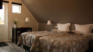 A bedroom with two beds, a desk, a chair, a potted plant, and a window. - Akkeri Guesthouse (Stykkisholmur)