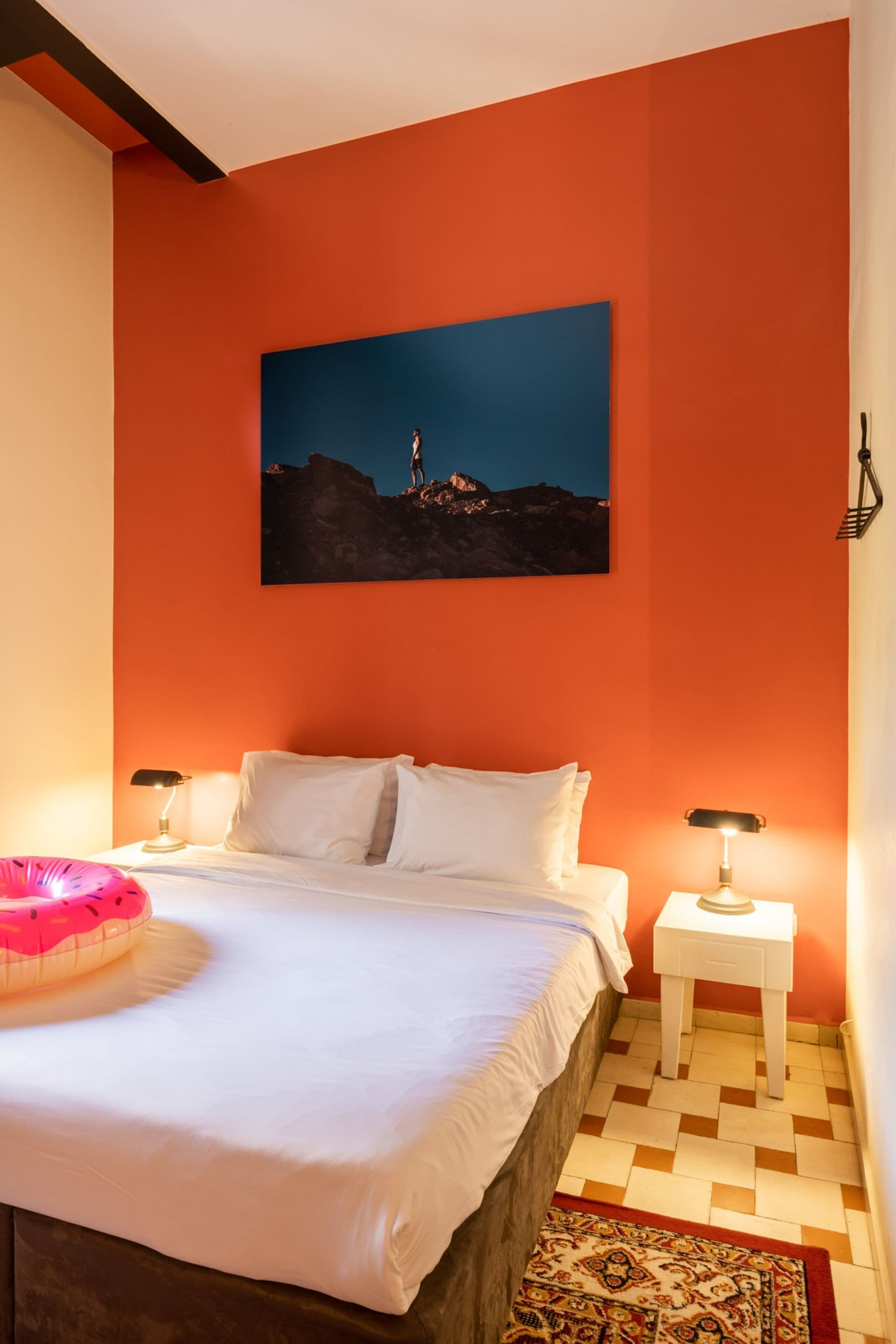 A bedroom with a bed, two bedside tables, a nightstand, a patterned rug, and a painting on the wall.