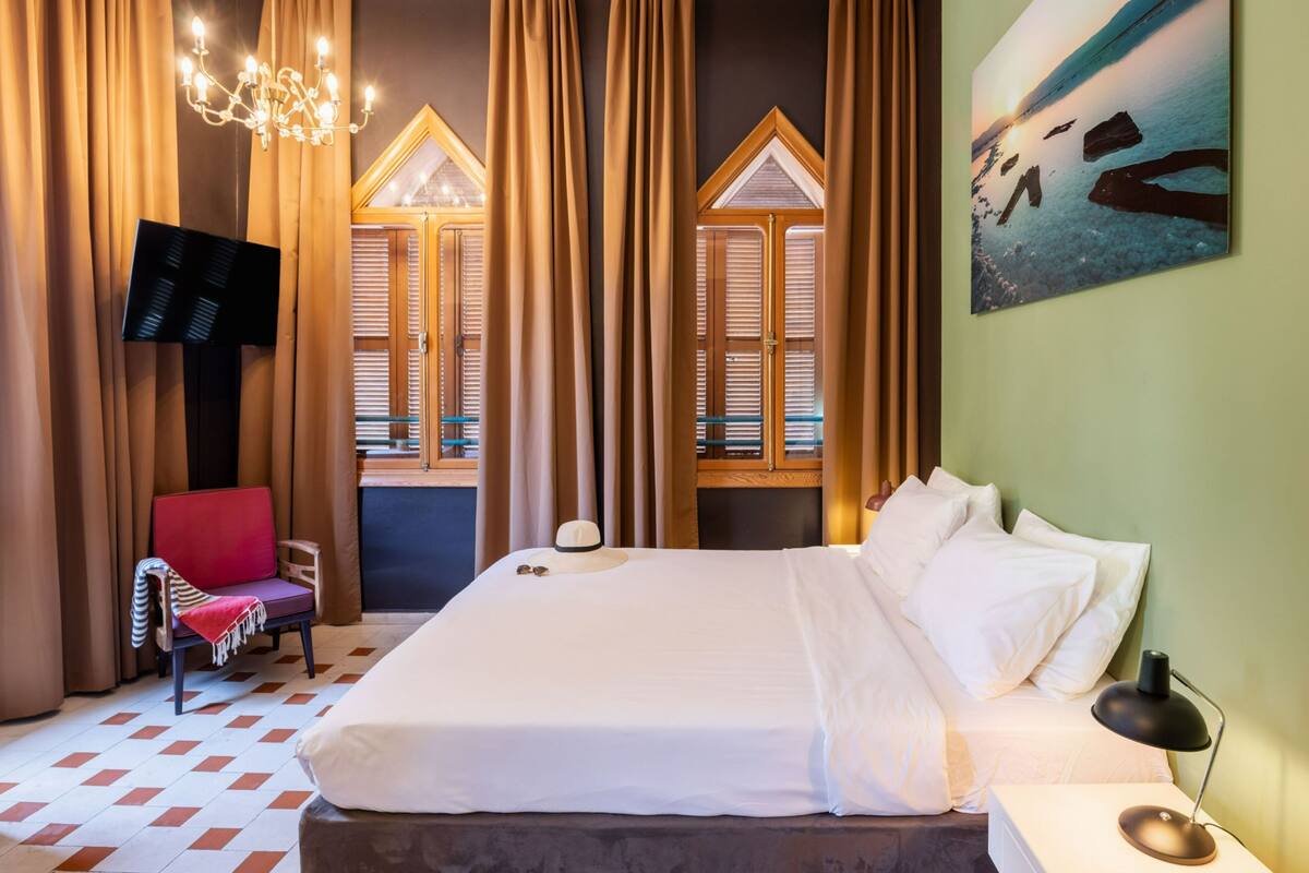 A hotel room with a large bed, a red chair, a TV, and a painting on the wall.