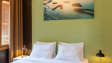 A neatly made bed with white linens, a painting of a sunset over water on the wall, and a patterned rug on the floor.
