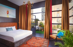A hotel room with a large bed, a view of the cityscape, and a balcony with a chair and plants. - INTA Hotel (Tel Aviv)