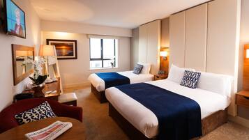 A hotel room with two beds, a desk with a chair, a TV, and a window.