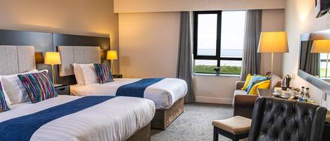 A hotel room with two beds, a sitting area with a chair, a table, and a view of the sea.