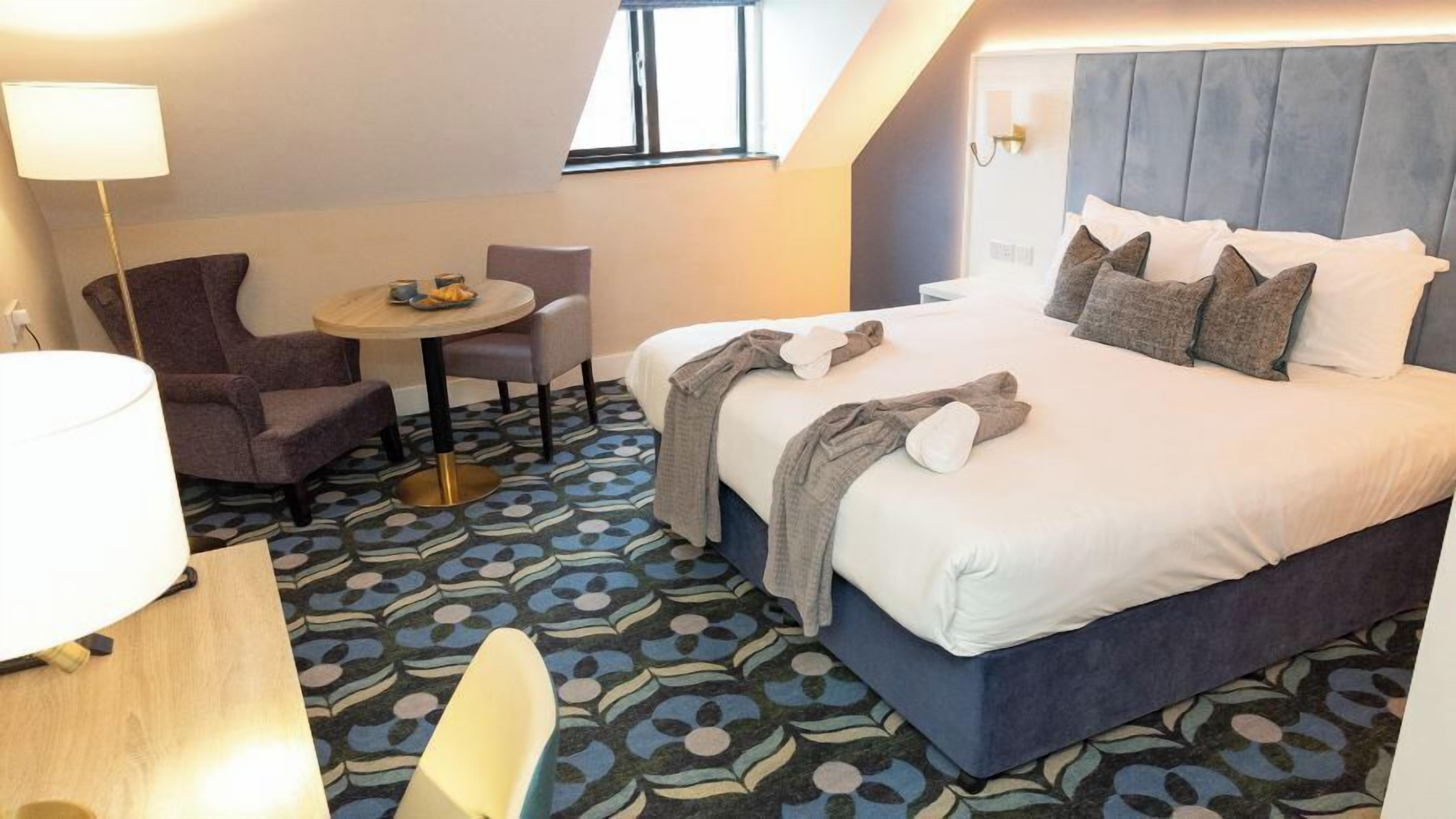 Una camera d'albergo con un letto, un tavolo rotondo con sedie, una lampada e una moquette decorata.