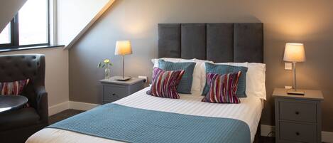 A modern hotel room with a large bed, two bedside tables, a chair, and a window.