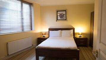 A hotel room with a large bed, two bedside tables with lamps, a framed picture on the wall, and a radiator under the window.